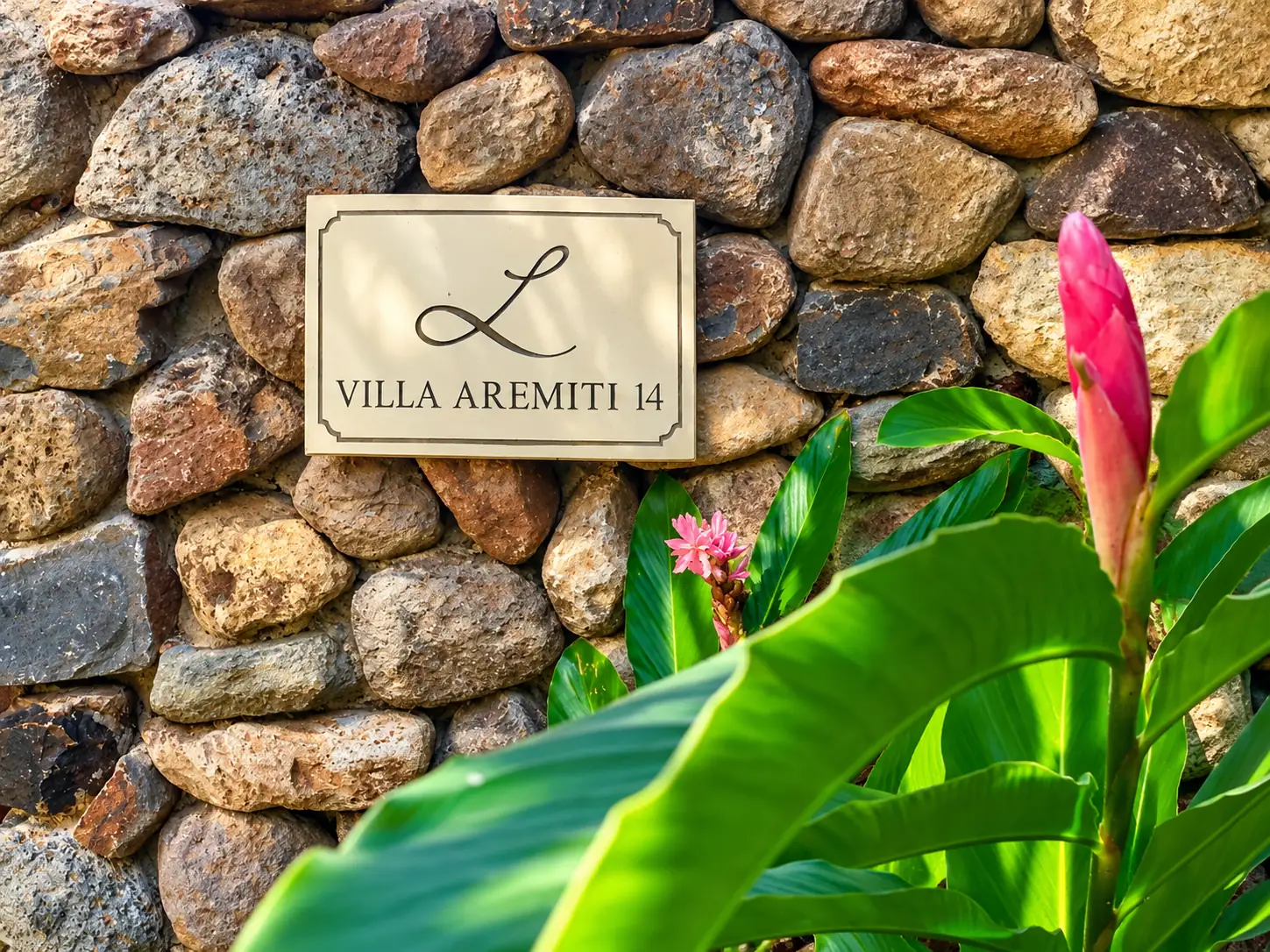 La plaque Villa Aremiti 14 sur un mur de pierre, entre les feuillages