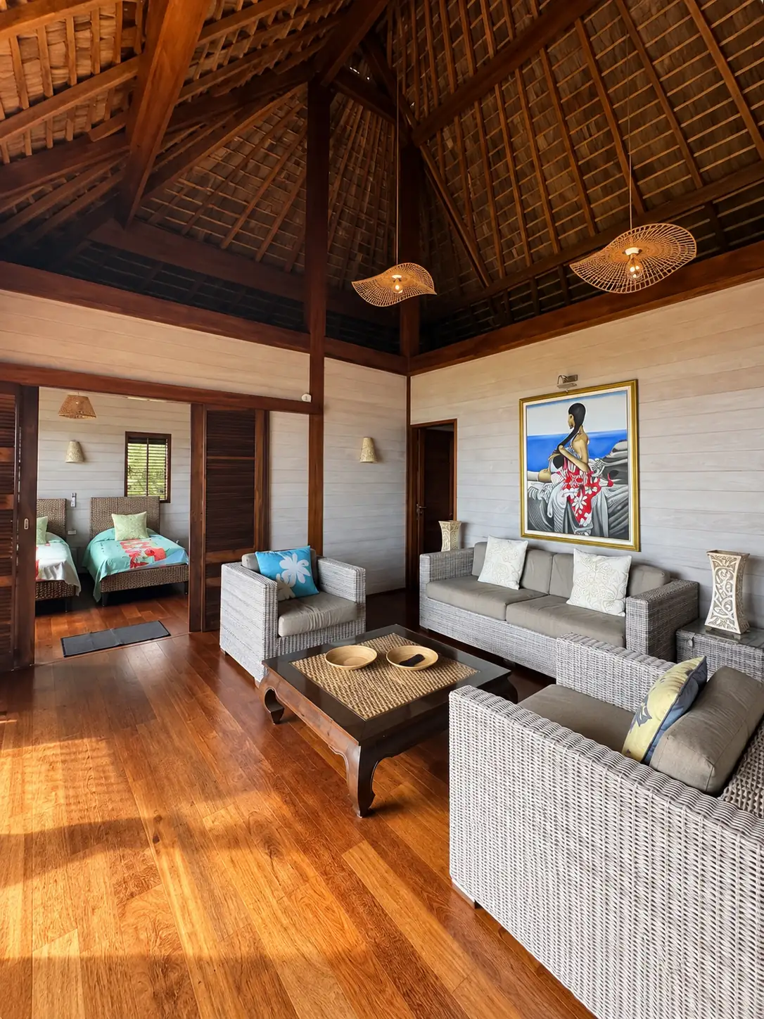 Le salon sous la charpente en pandanus, canapés et tableau de vahiné
